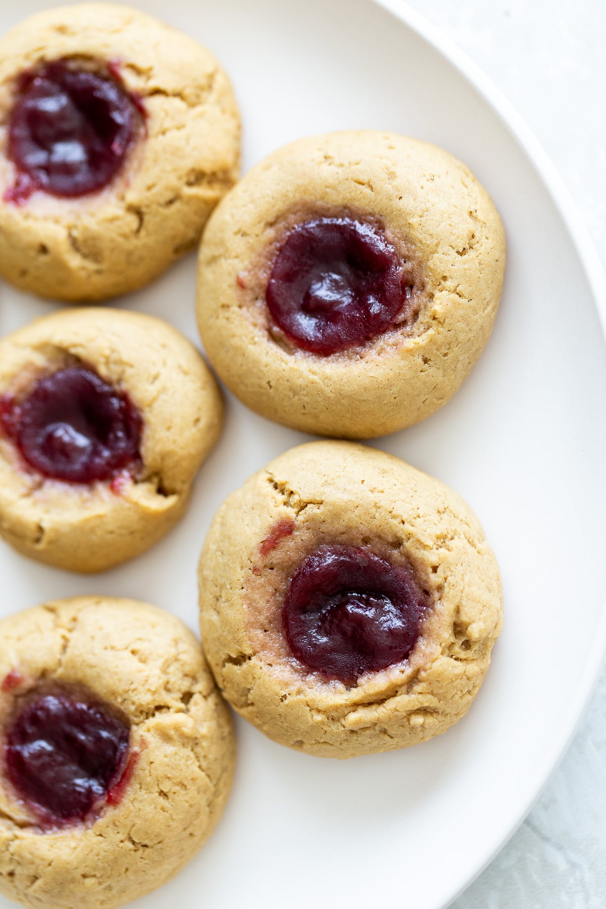 overhead shot of vegan pb & j thumbprint cookies on a white plate 