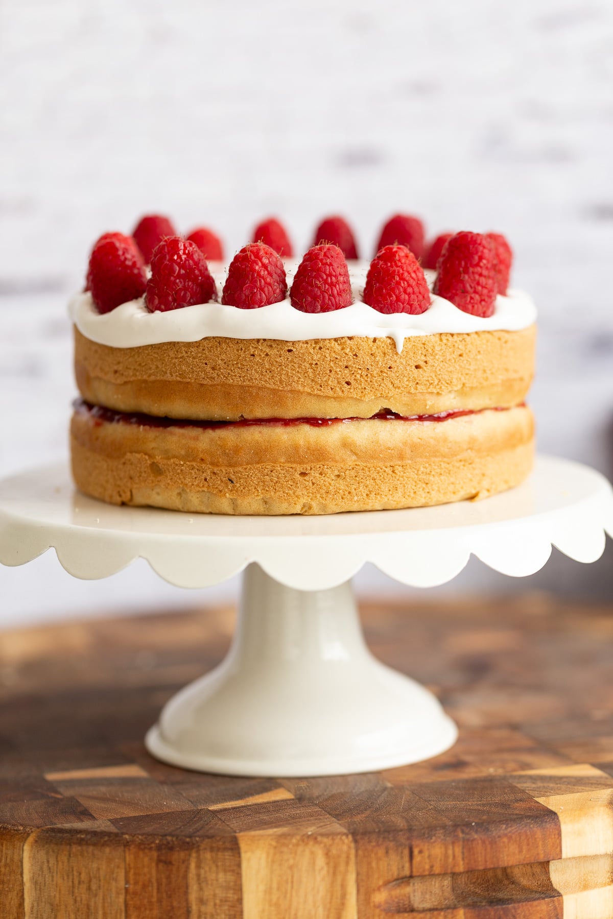 vegan white cake a vegan white cake topped with coconut whip and raspberries on a white cake stand