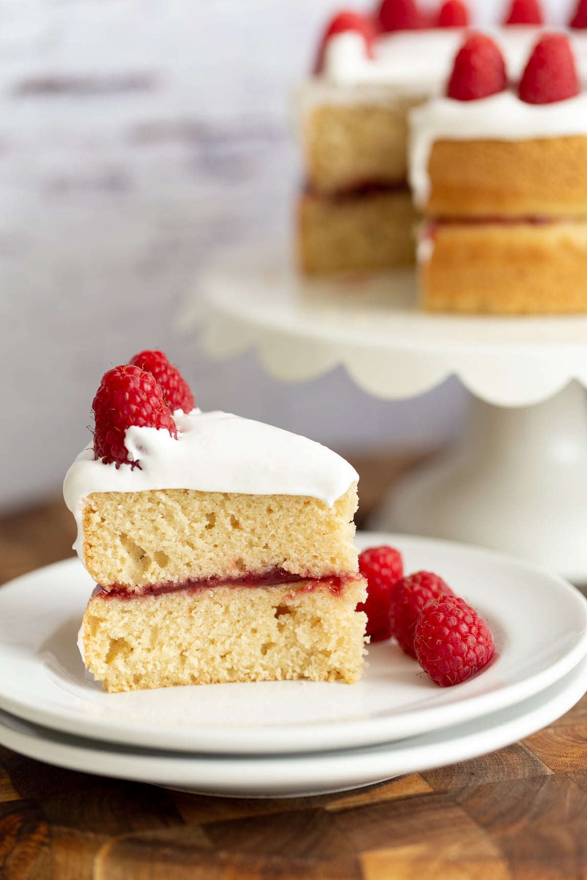vegan white cake a jam filled and coconut whip topped slice of vegan white cake with fresh raspberries on a white plate