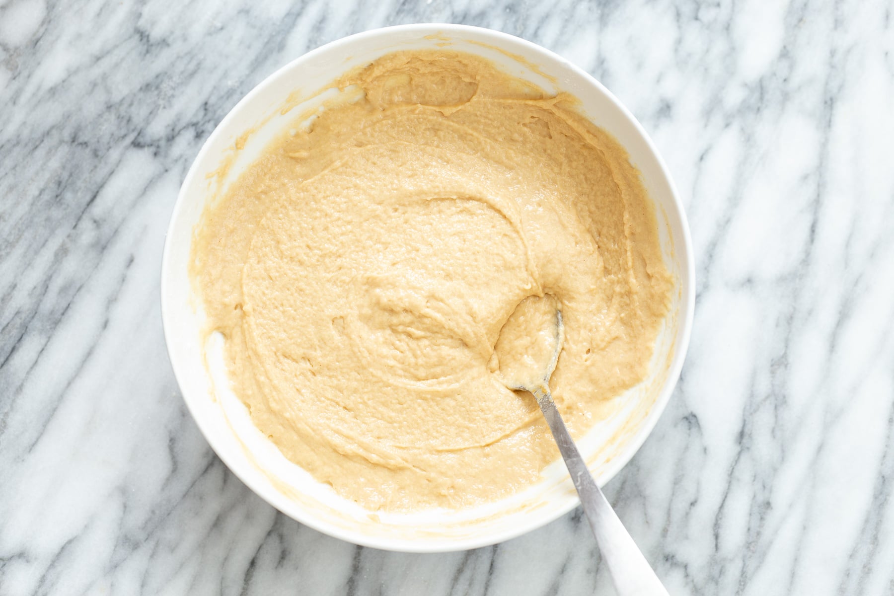 peanut butter and jelly cake peanut butter cake batter being mixed with a metal spoon in a white mixing bowl