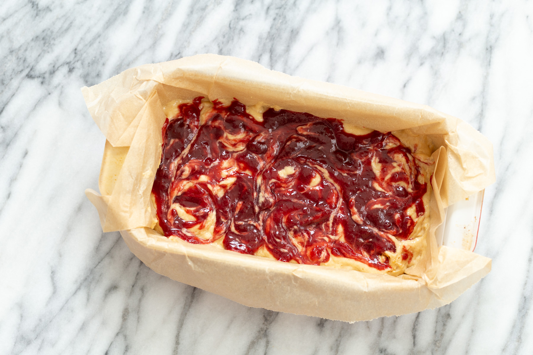 peanut butter and jelly cake raspberry jam being swirled into peanut butter cake batter