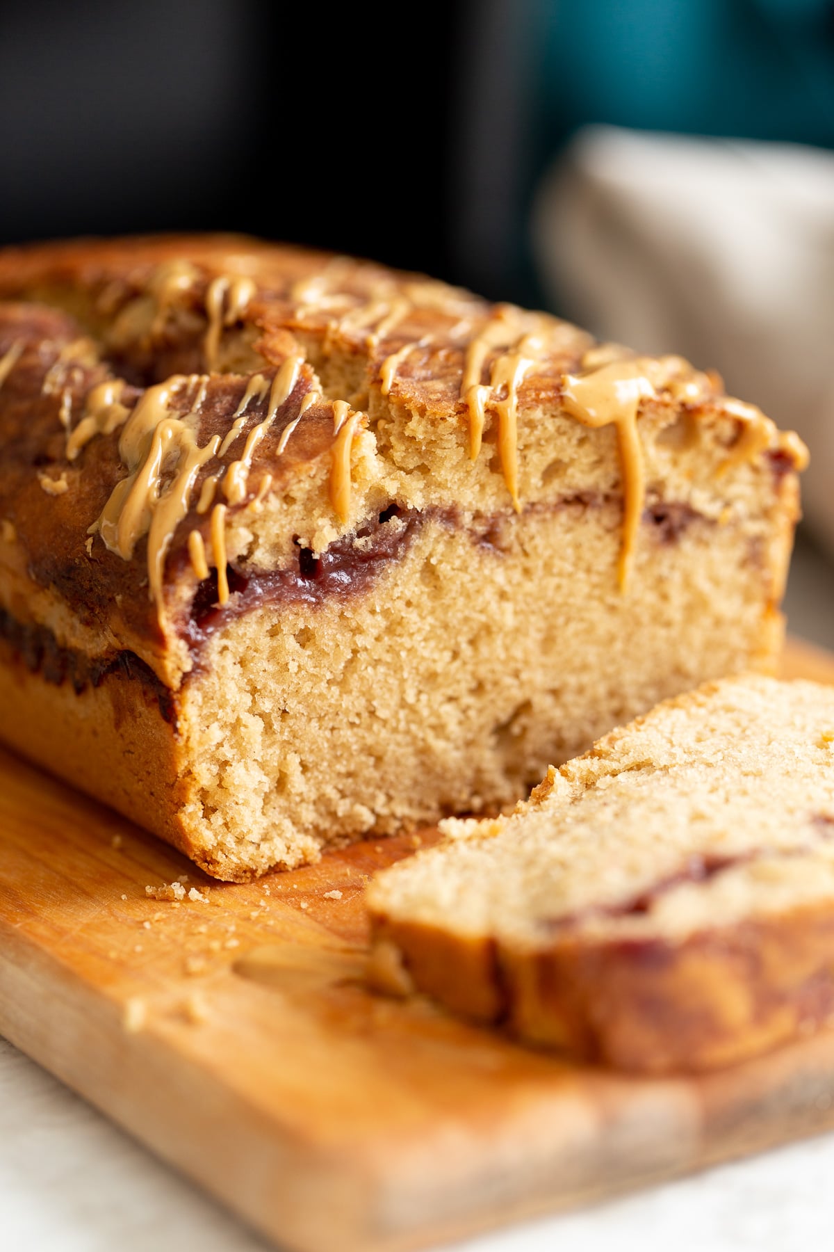 peanut butter and jelly cake close up of a sliced vegan pb and j loaf cake drizzled with peanut butter on a cutting board