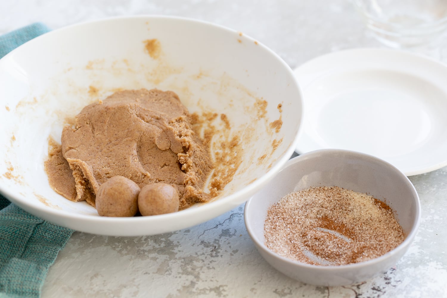 energy bites snickerdoodle bites being rolled in a bowl with some cinnamon sugar for coating on the side