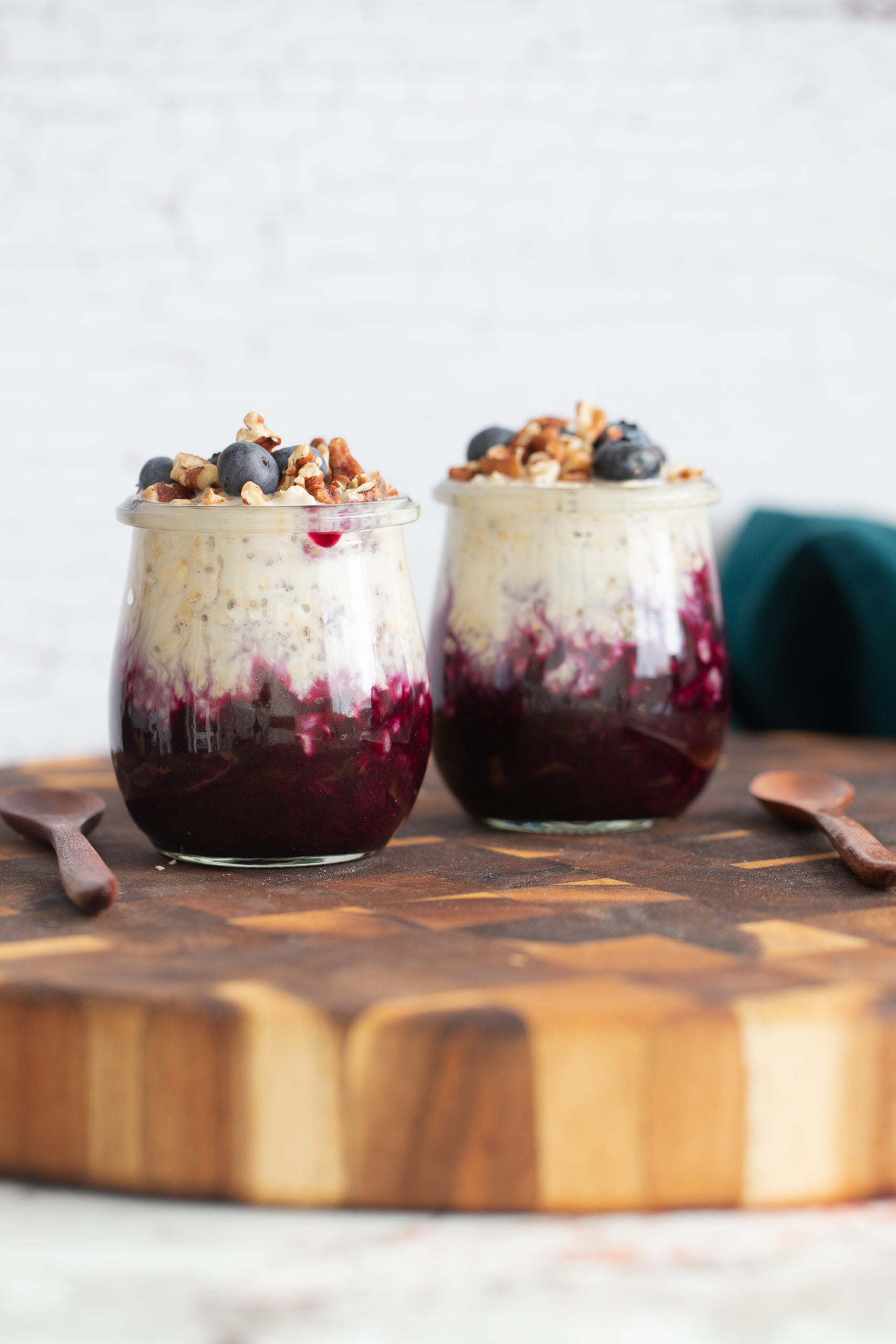 side view of two jars of make ahead vegan blueberry muffin overnight oats on wooden board