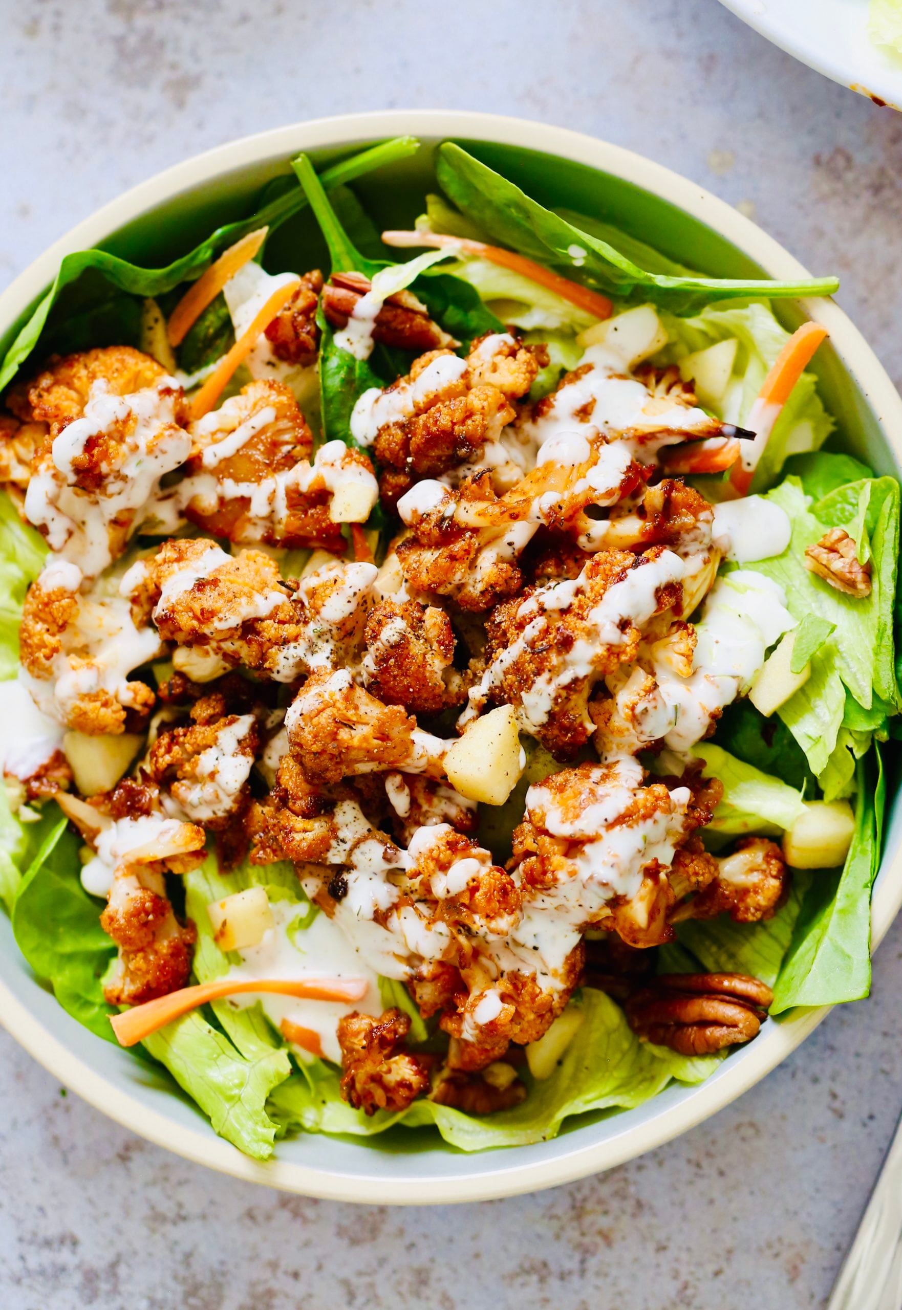 overhead shot of a salad bowl topped with bbq roasted cauliflower and vegan ranch dressing
