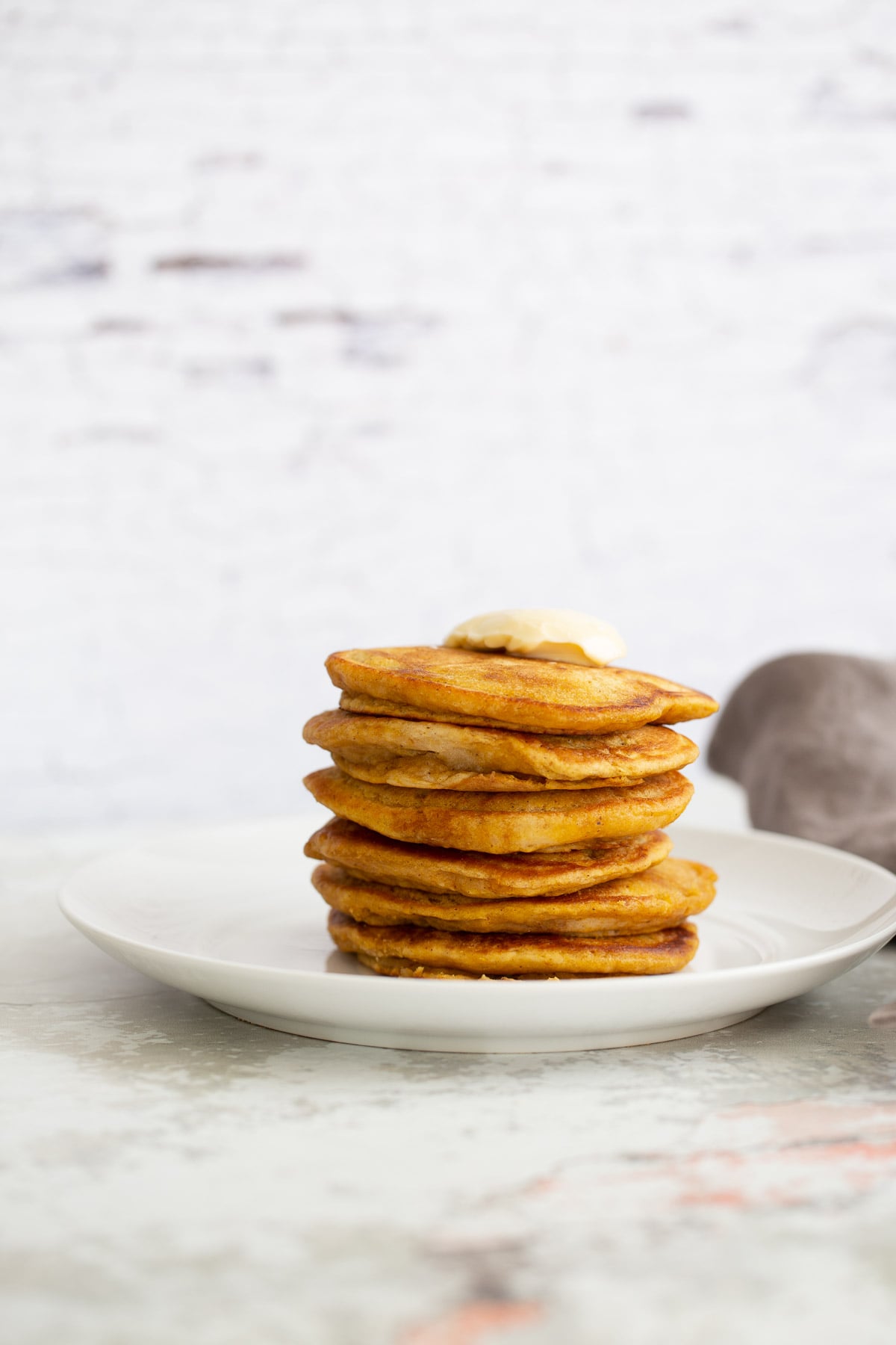 a stack of vegan pumpkin pancakes against a white brick wall 