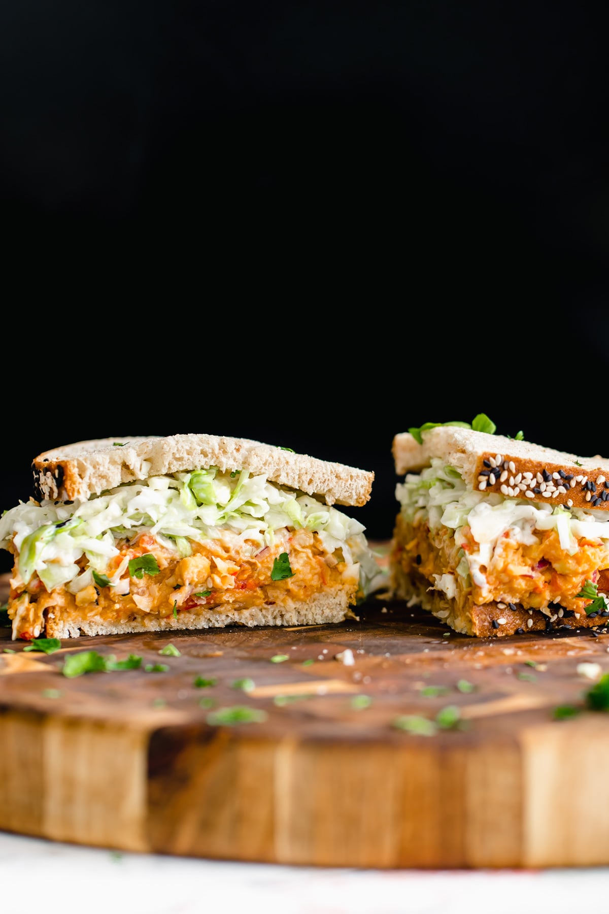 chickpea salad sandwich a halved buffalo chickpea salad sandwich with slaw on a wooden chopping board
