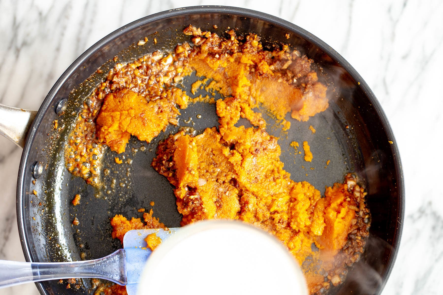 pumpkin curry pumpkin puree being added to pan with tempered Indian spices