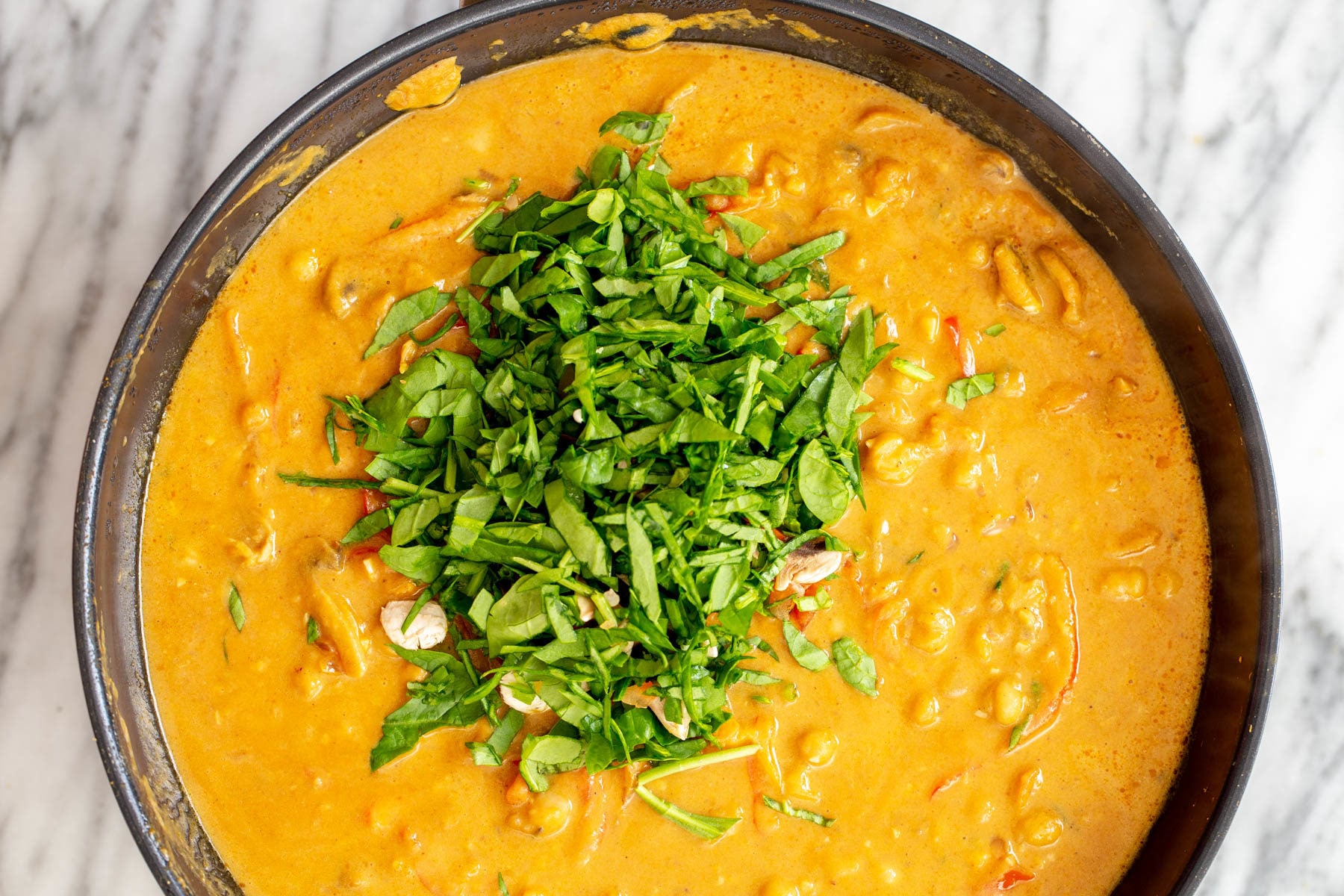 pumpkin curry pumpkin chickpea curry being sprinkled with fresh herbs before serving