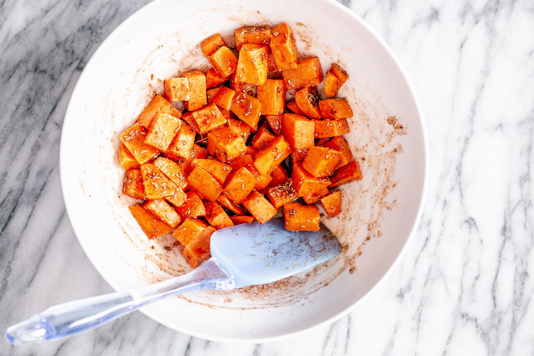 Thanksgiving sheet pan dinner sweet potato cubes being tossed in a white bowl