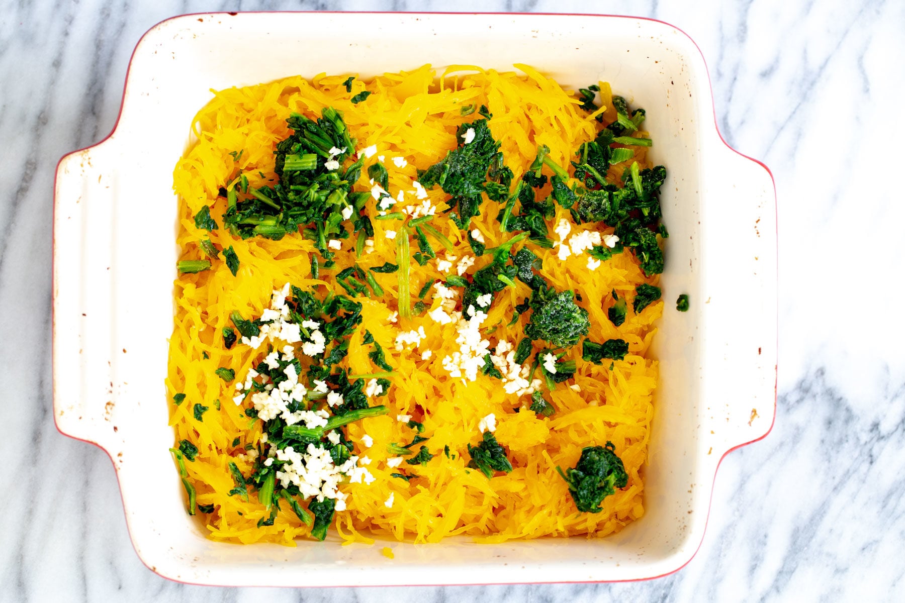 cooked spaghetti squash, spinach and garlic in a white casserole dish 