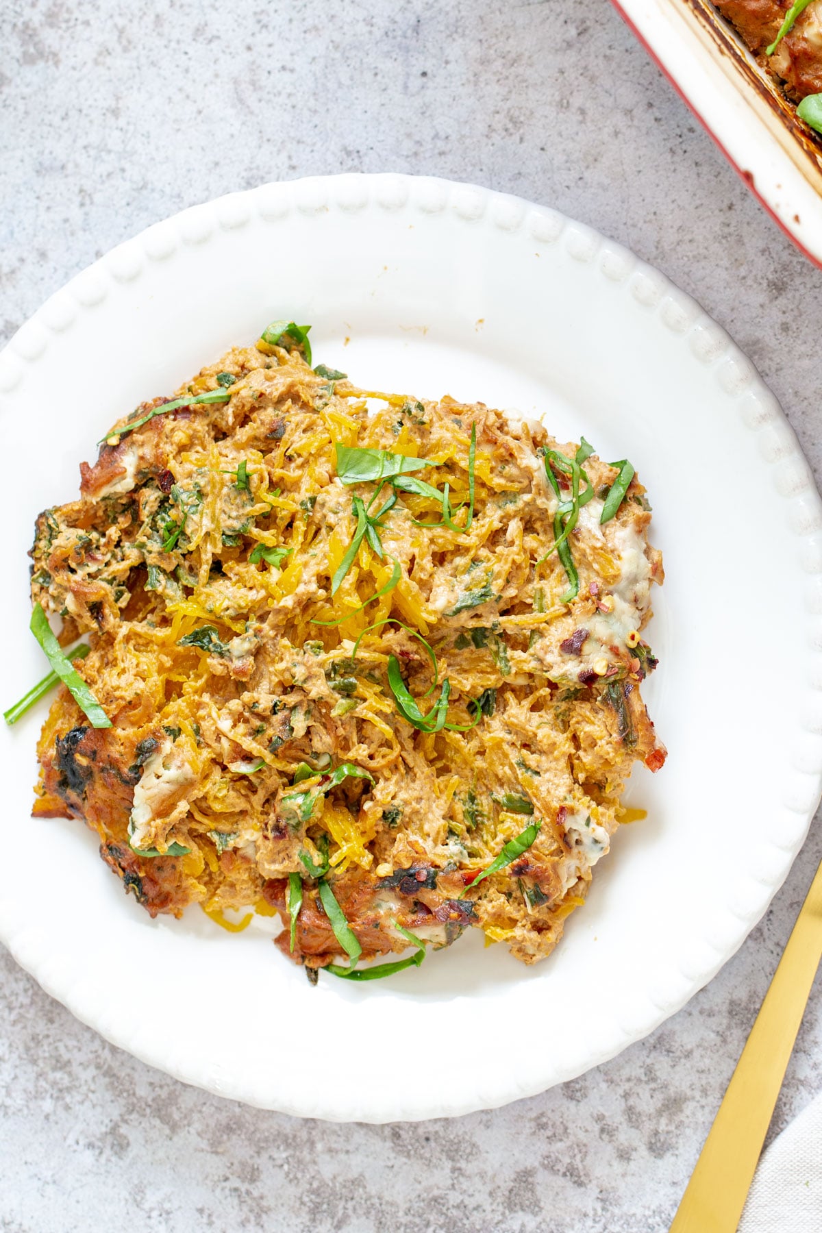 a serving of vegan spaghetti squash pasta bake on a white plate with a golden fork 