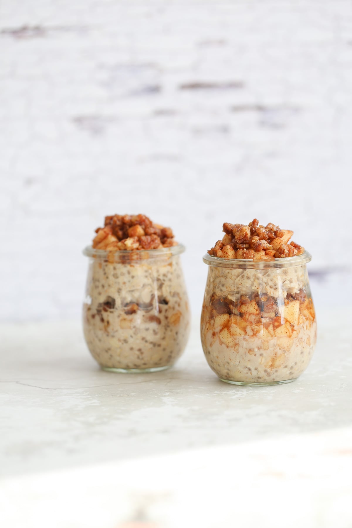 apple pie overnight oats side view of two jars of apple pie overnight oats topped with stewed apples and candied pecans