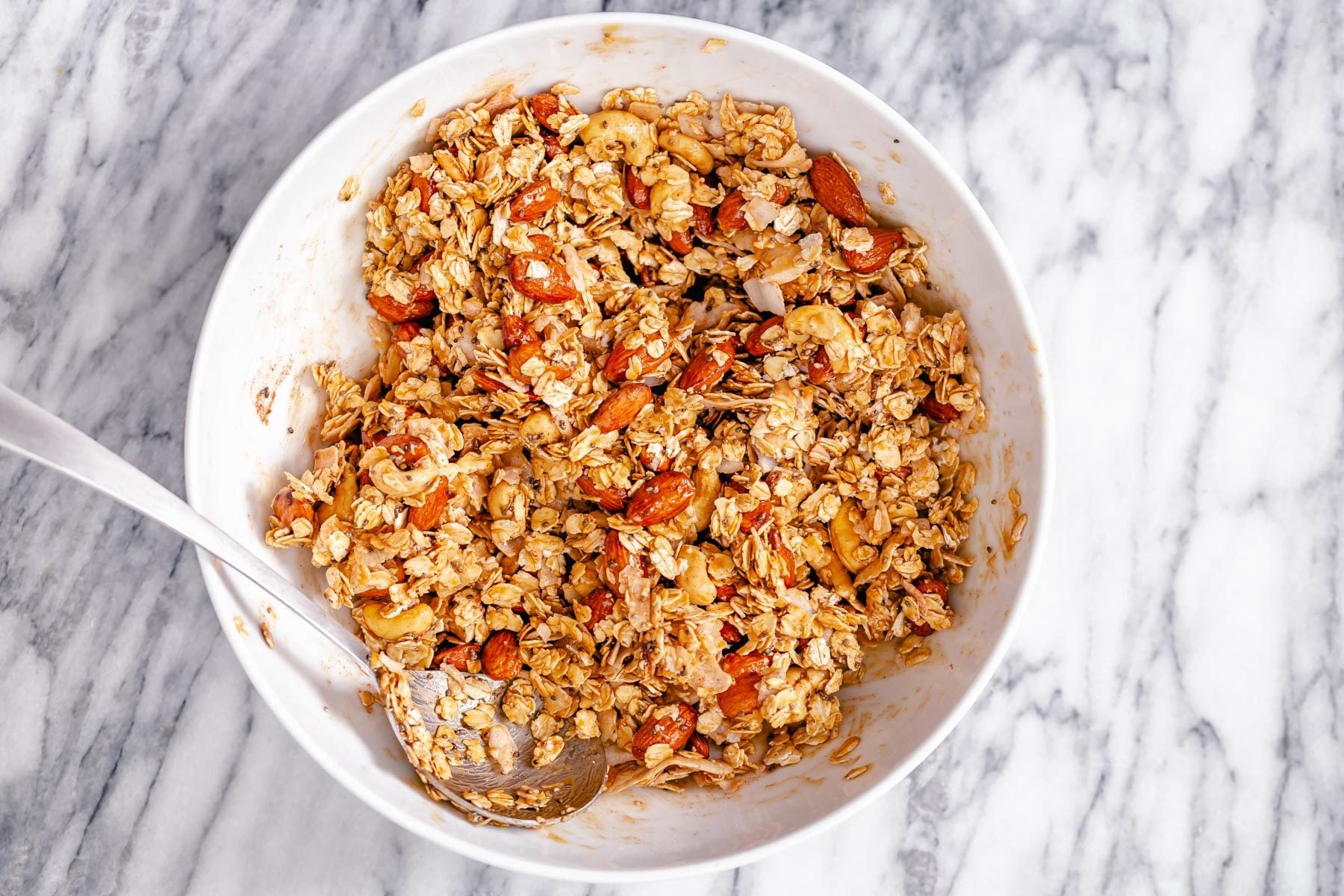 coconut granola almond coconut granola being mixed in a small white bowl
