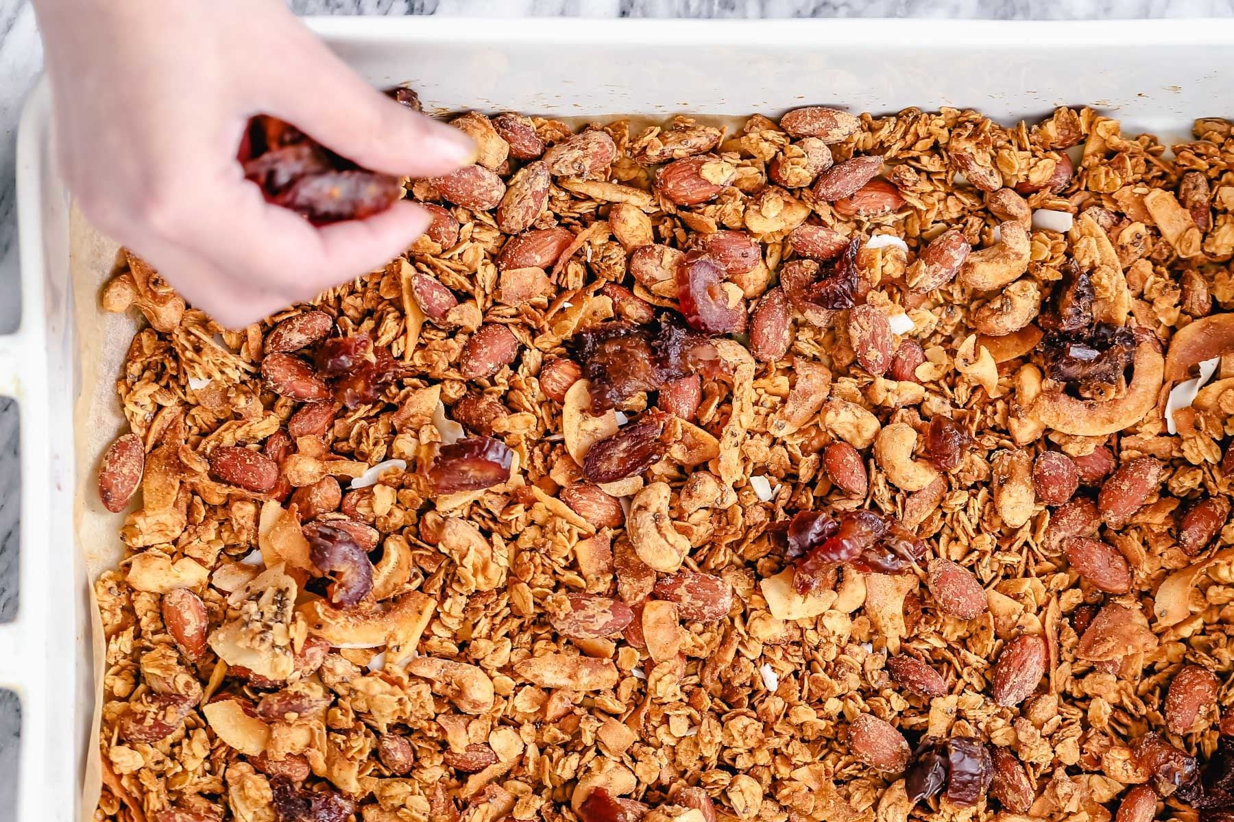 coconut granola baked vegan granola being spread out in a casserole dish