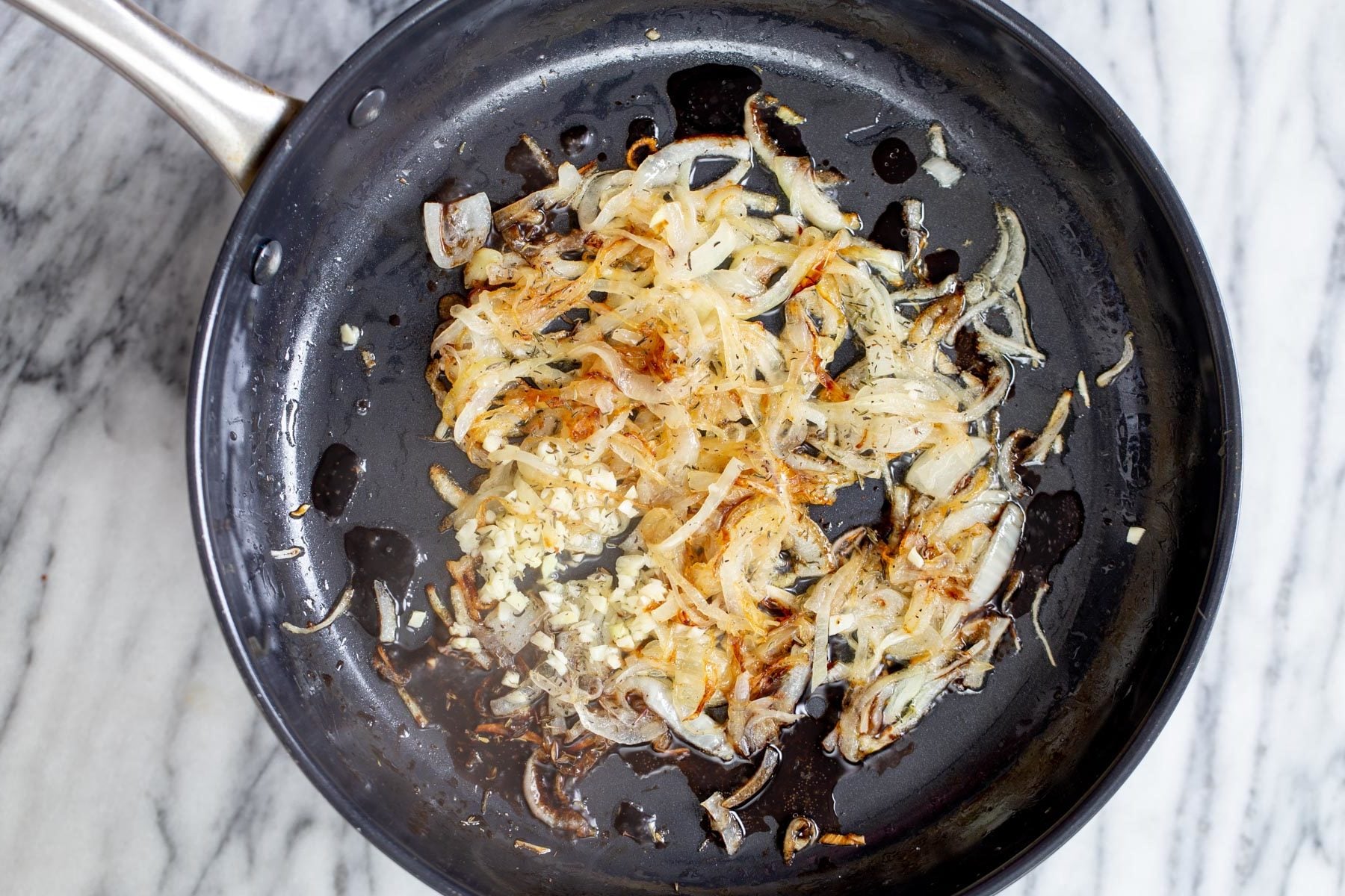 Vegan Skillet Lasagna garlic being added to caramelized onion slices in a skillet