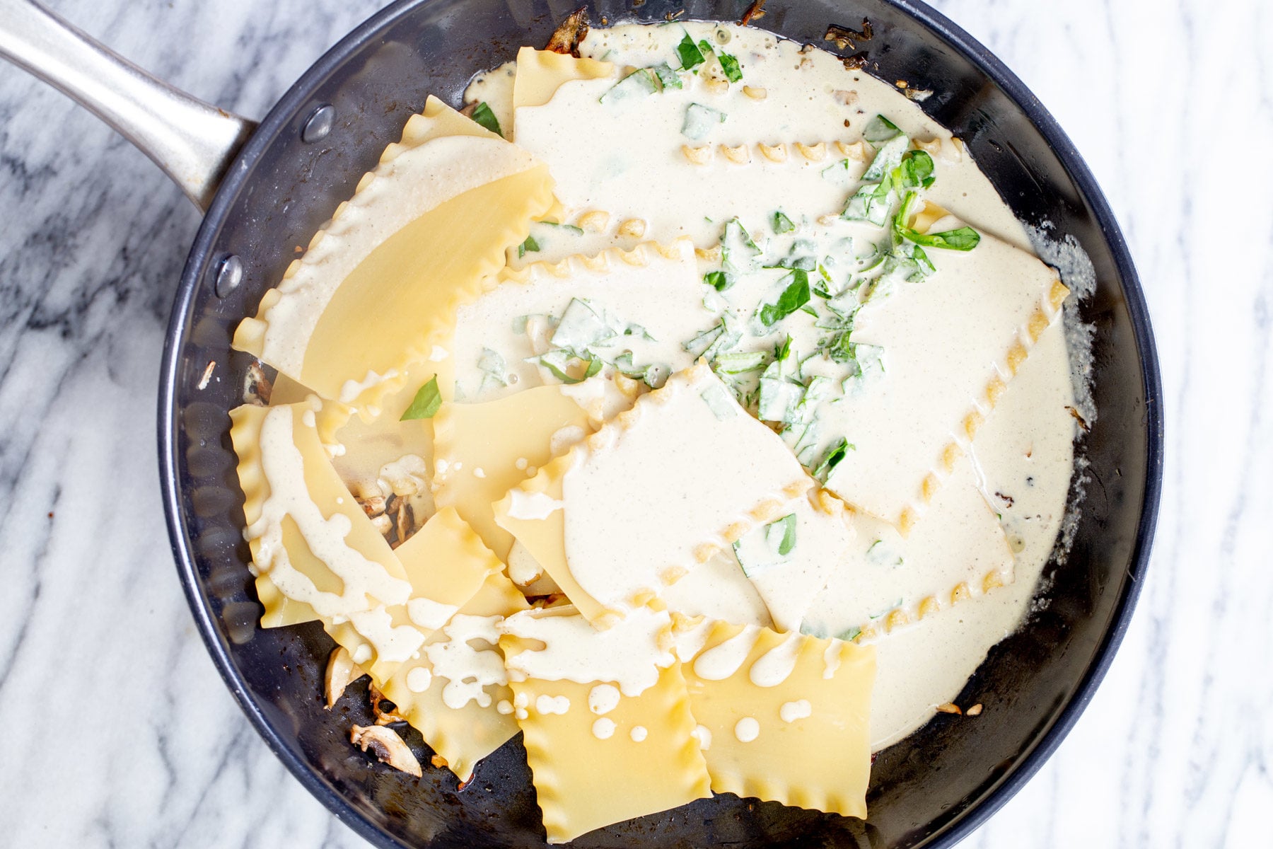 vegan skillet lasagna vegan bechamel sauce being added to lasagna noodles and caramelized onion is a pan