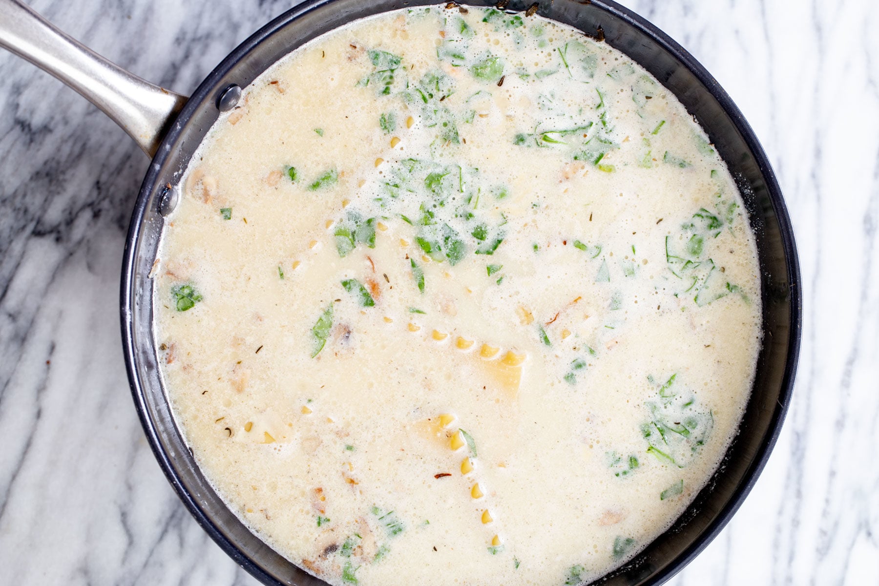 overhead shot of a skillet with lasagna pasta cooking in vegan bechamel