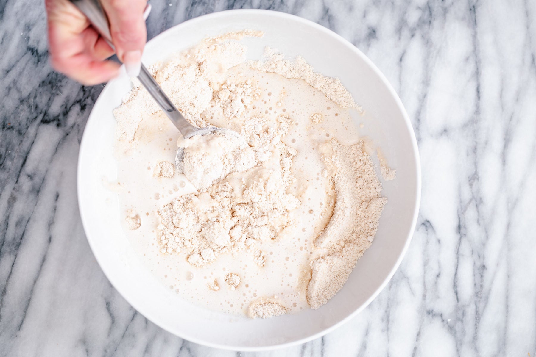 glutenfree donuts recipe wet ingredients being stirred into dry donut ingredients in a white bowl