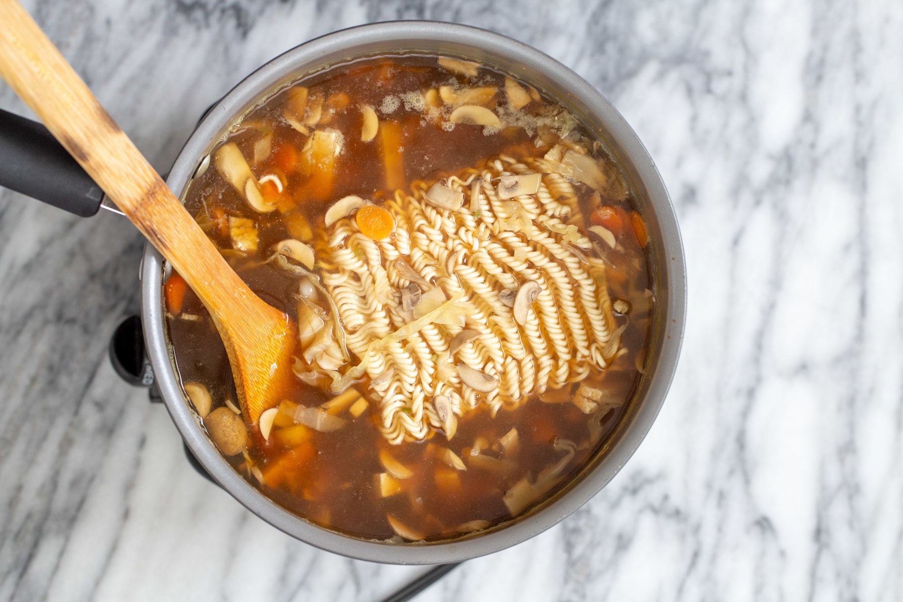 vegan hot and sour soup ramen noodles being added to a pot of vegan hot and sour ramen soup