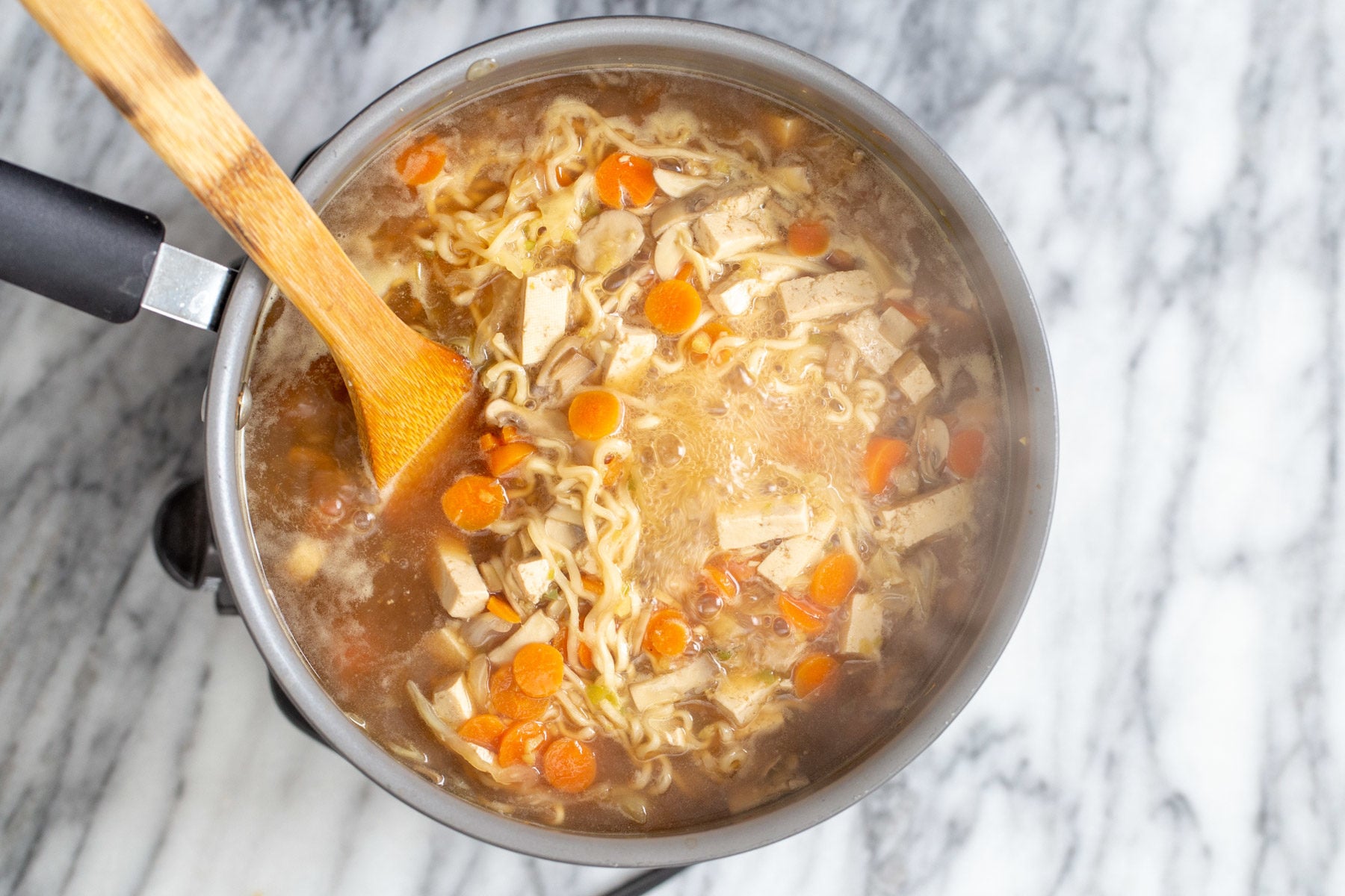 vegan hot and sour soup a wooden spoon stirring in a pot with vegan hot and sour soup with ramen noodles