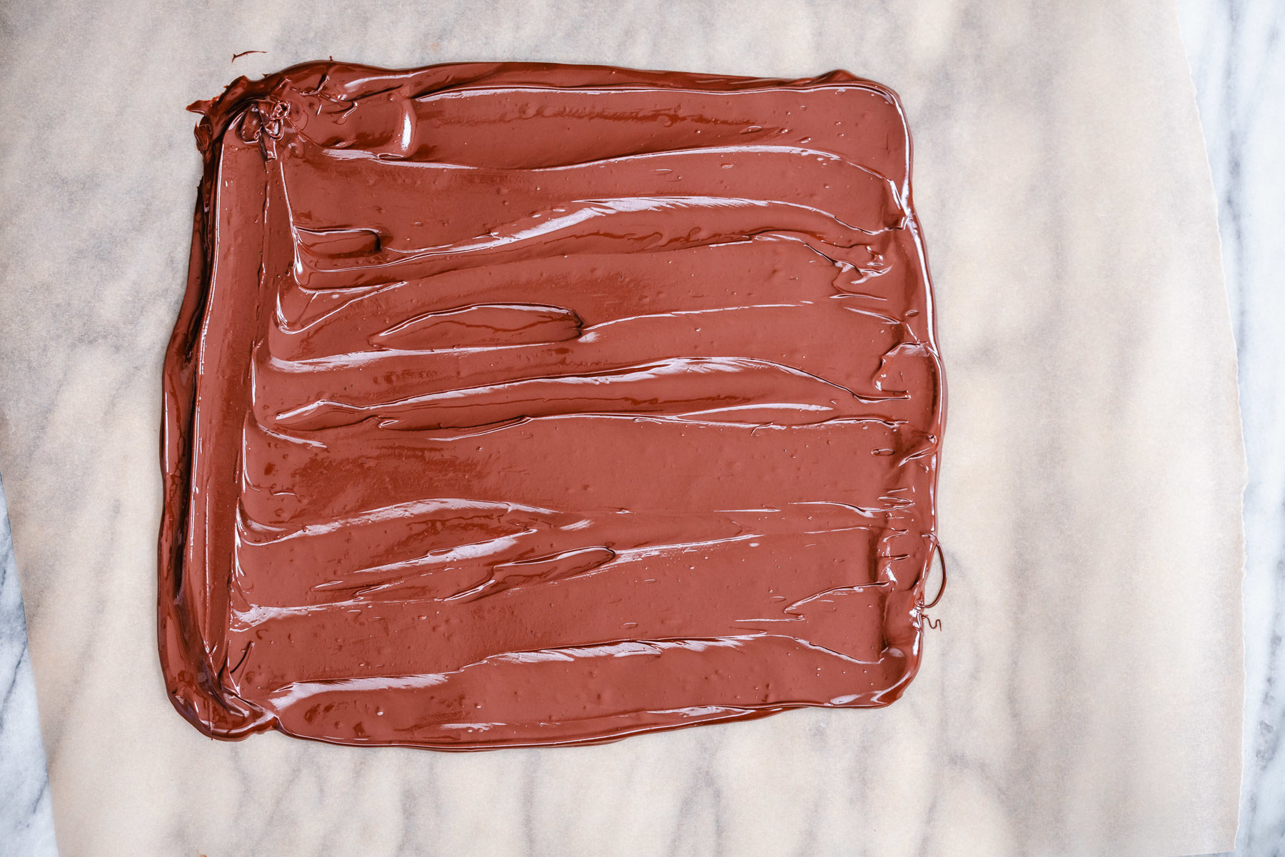 peanut butter chocolate bark melted chocolate being spread out into a rectangle to make chocolate bark