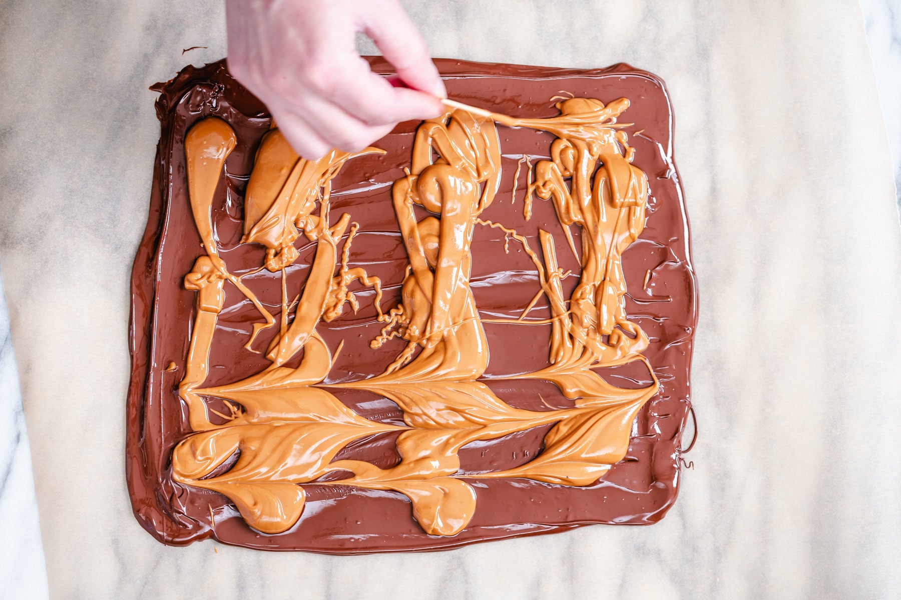 peanut butter chocolate bark melted peanut butter being swirled into a rectangle of melted chocolate to make chocolate bark