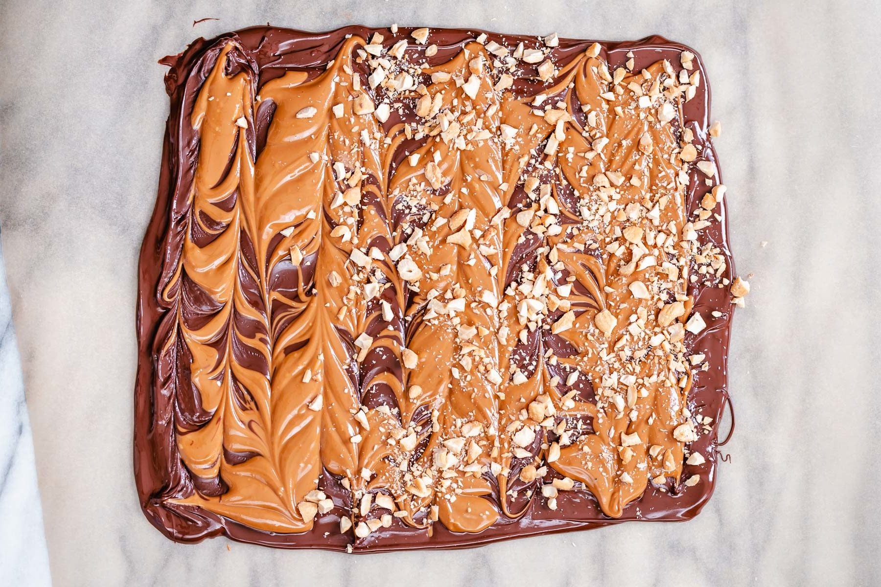 peanut butter chocolate bark chopped peanuts being sprinkled on top of vegan peanut butter chocolate bark