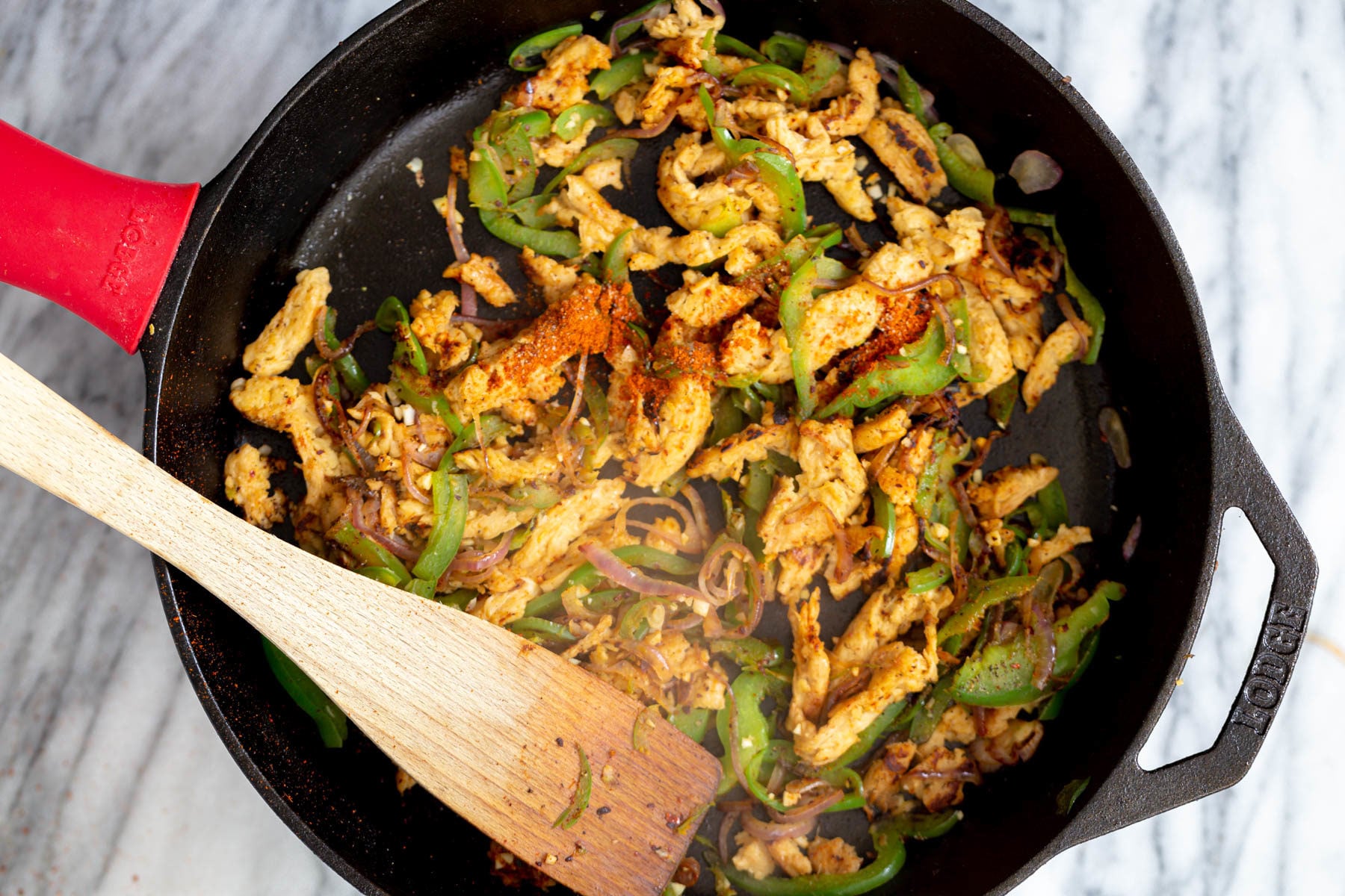 vegan skillet enchiladas spices being added to sauteed veggies and soy curls in a black skillet
