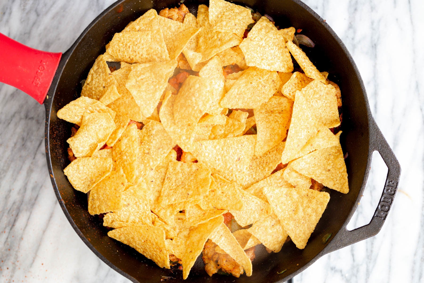 tortilla chips being layered on top of Mexican soy chunk veggie filling for making enchiladas