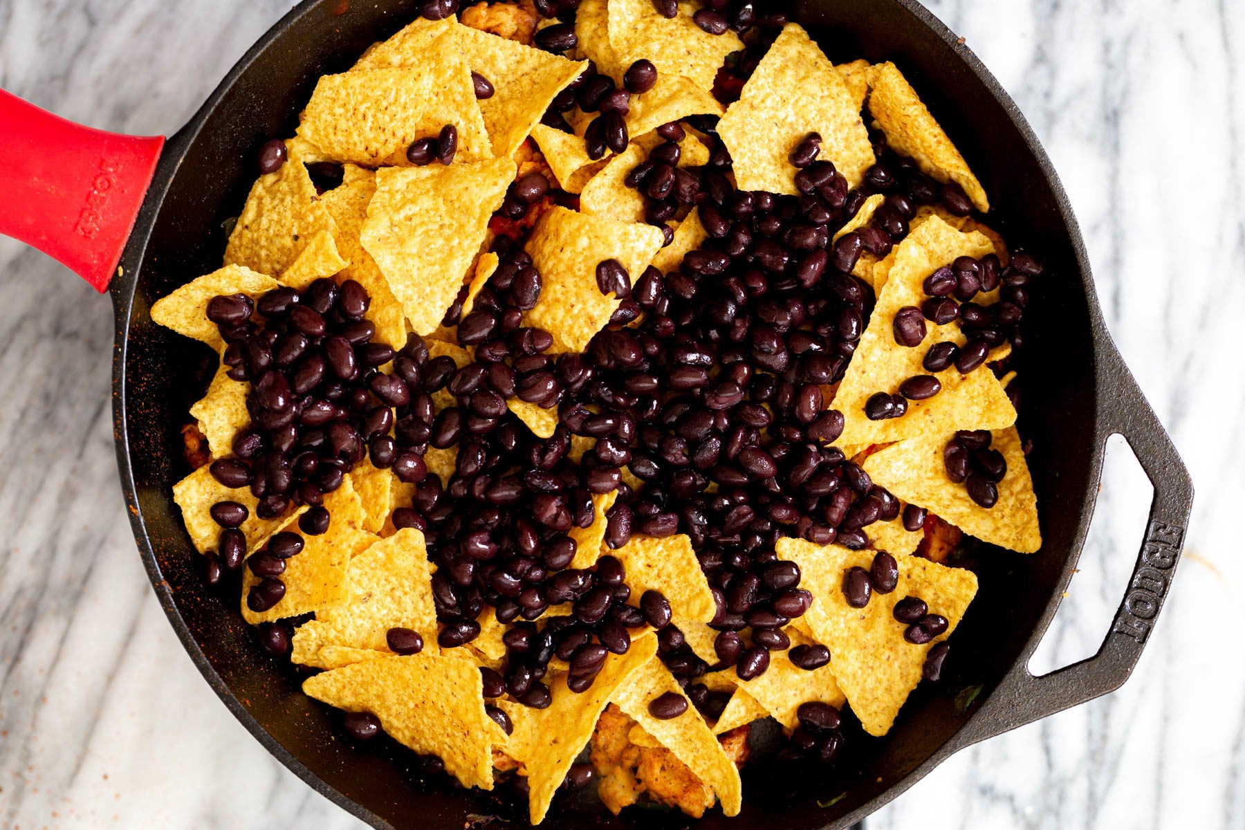 black beans being added on top of tortilla chips for making enchiladas