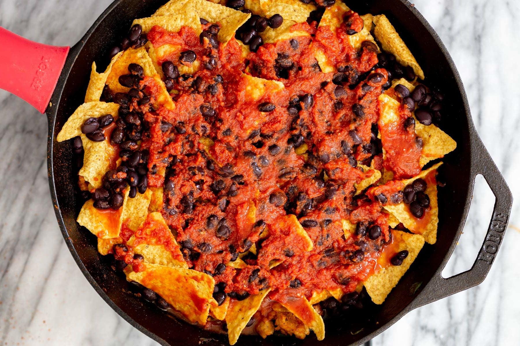 vegan red sauce being layered with tortilla chips and black beans for making vegan skillet enchiladas