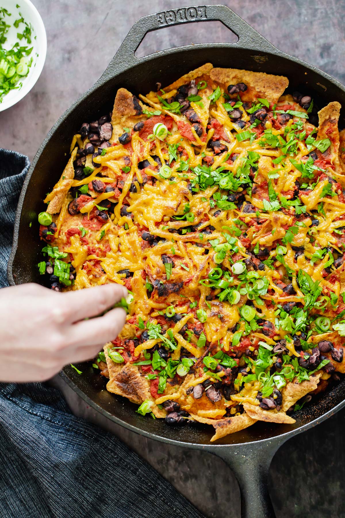 vegan skillet enchiladas a hand reaching for a serving of vegan skillet enchiladas with black beans