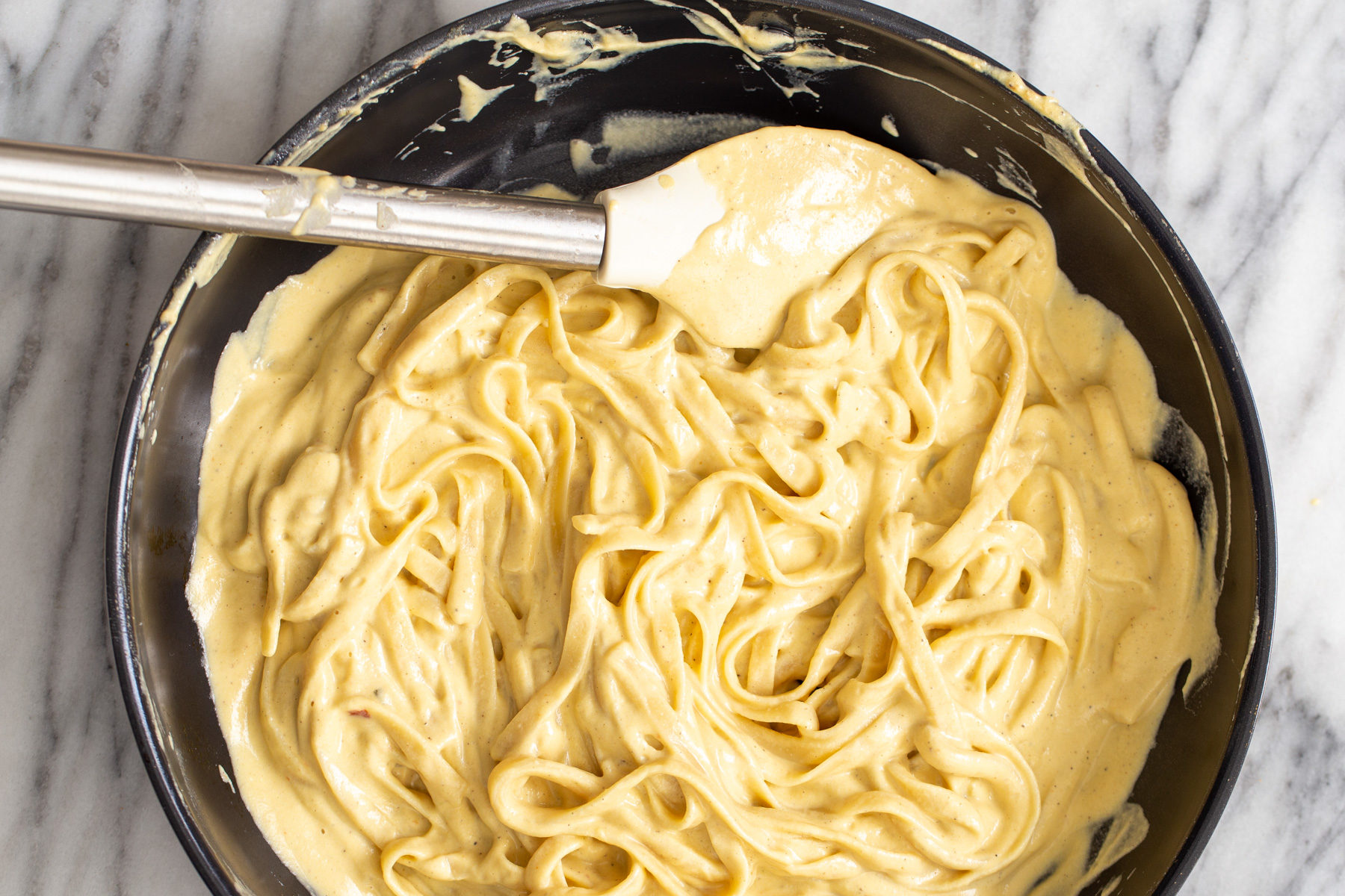 butternut squash carbonara fettuccine being tossed in vegan butternut squash cashew cheese carbonara sauce