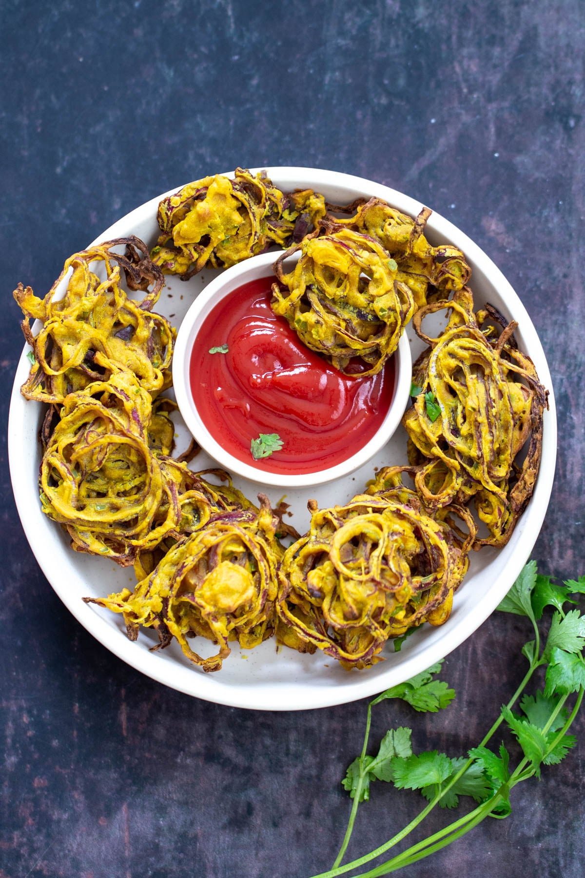 baked pakora baked vegan onion bhaji arranged on a white platter with a small dish of ketchup in the middle
