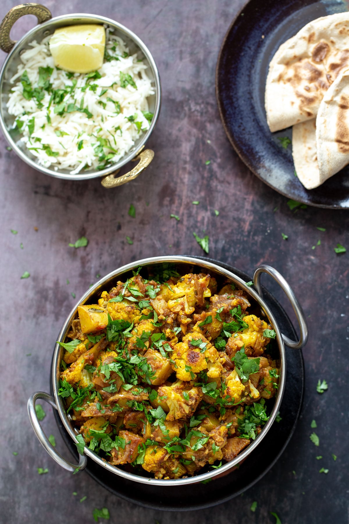 vegan aloo gobi a small pot of rice and an indian dish with vegan aloo gobi on a wooden surface