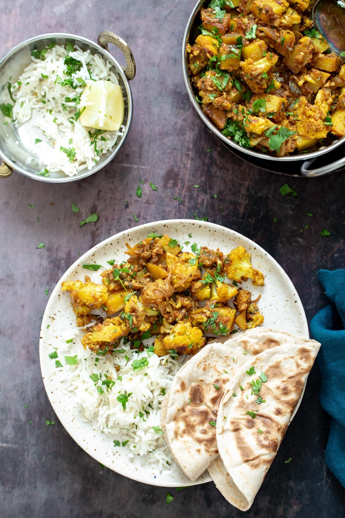 vegan aloo gobi a plate with a serving of aloo gobi, rice and 2 folded naan breads