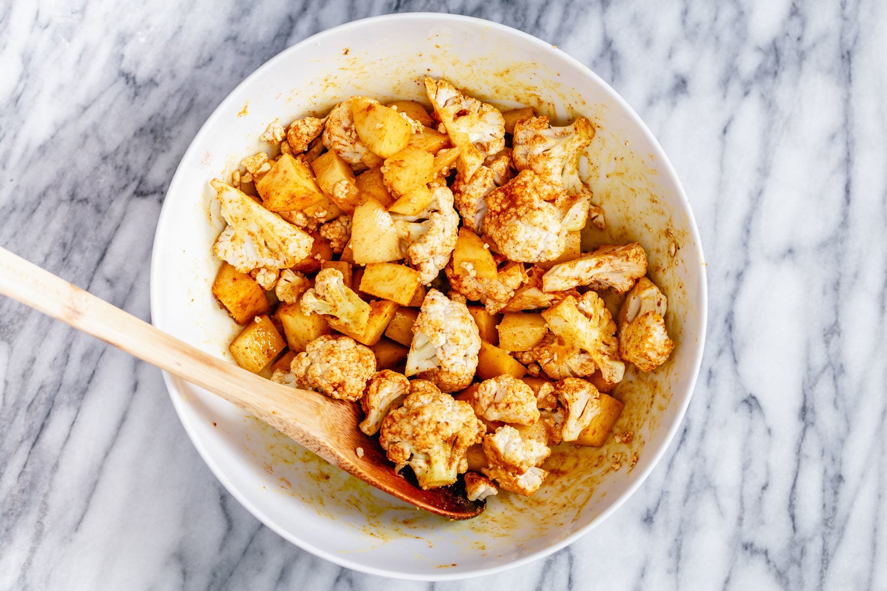 vegan aloo gobi a white bowl with cauliflower and potato cubes being tossed with Indian spices
