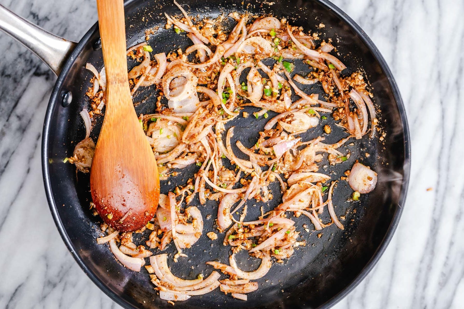 vegan aloo gobi onion ginger and garlic being sauteed with spices in a large frying pan