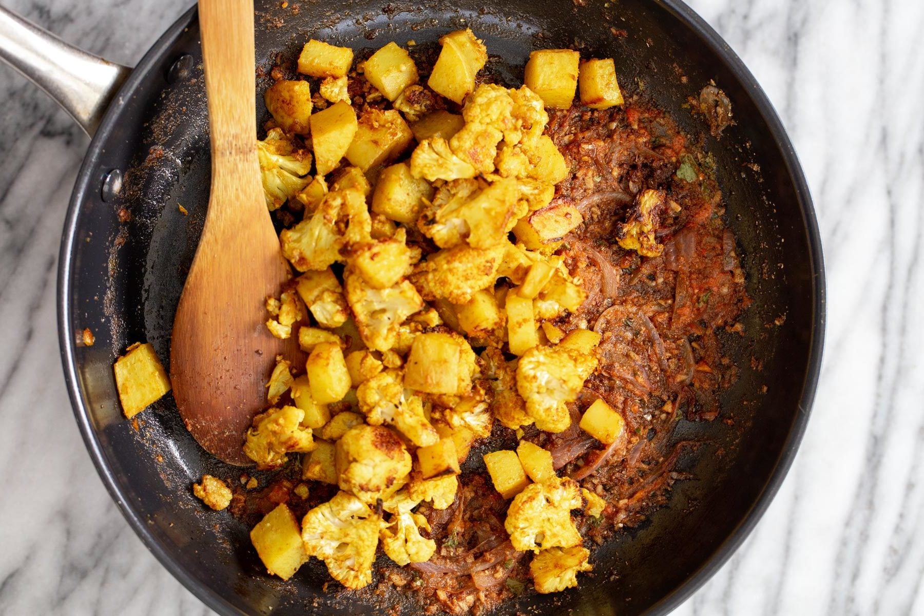 vegan aloo gobi cauliflower and potato cubes being tossed with sauteed spices
