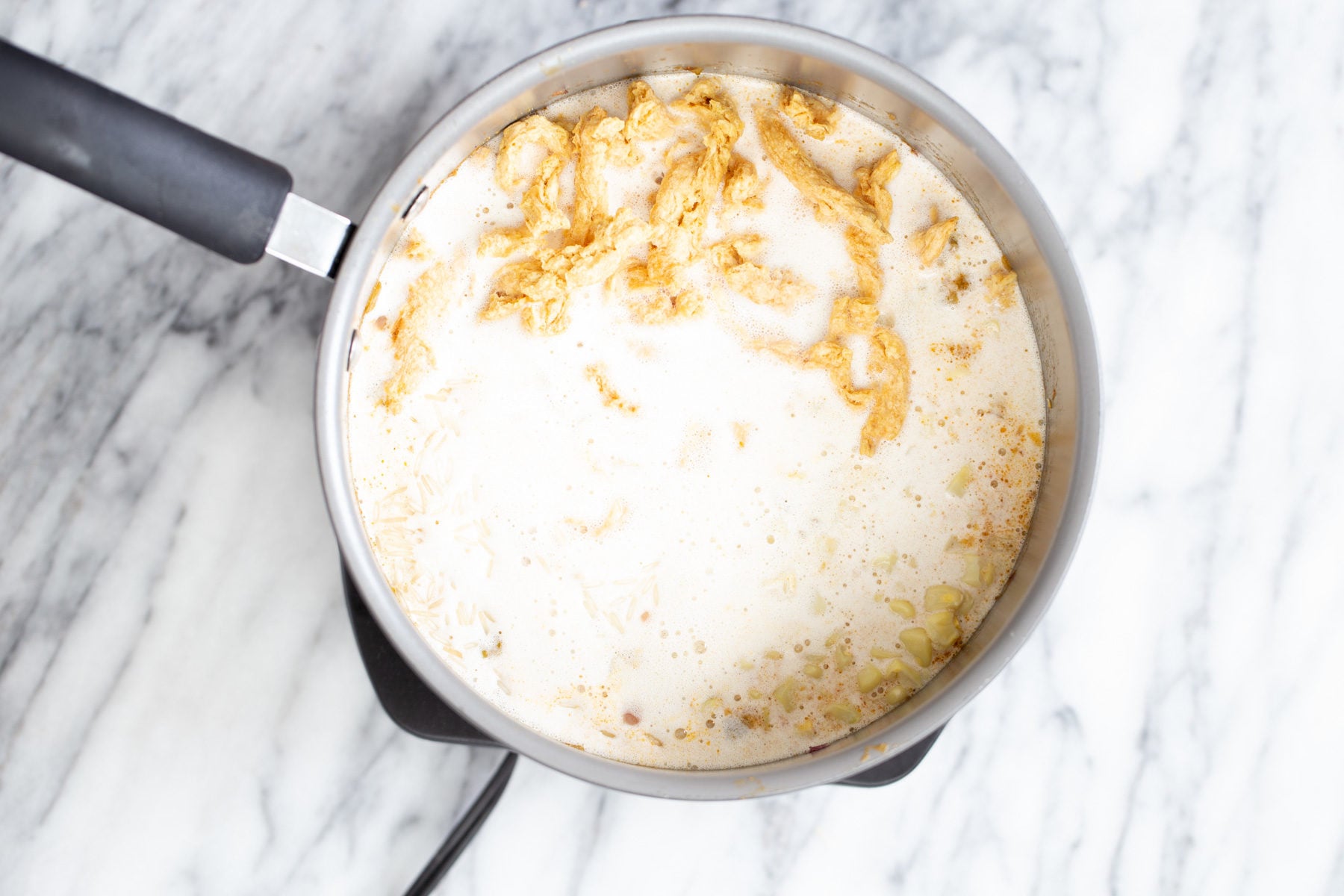 cashew cream being added to a pot with soy chunks corn and chile