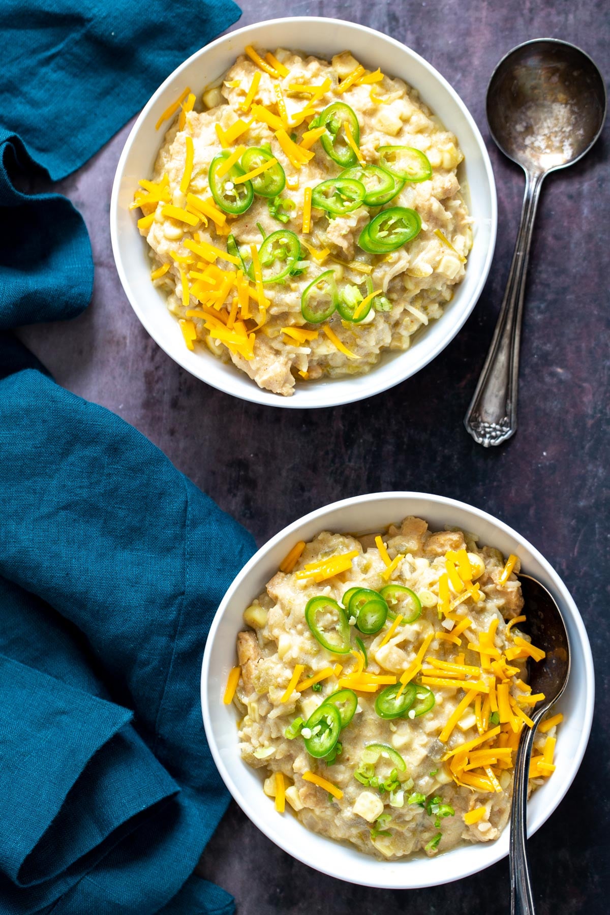 two bowls of vegan green chile enchilada soup with shredded cheese and sliced green chiles