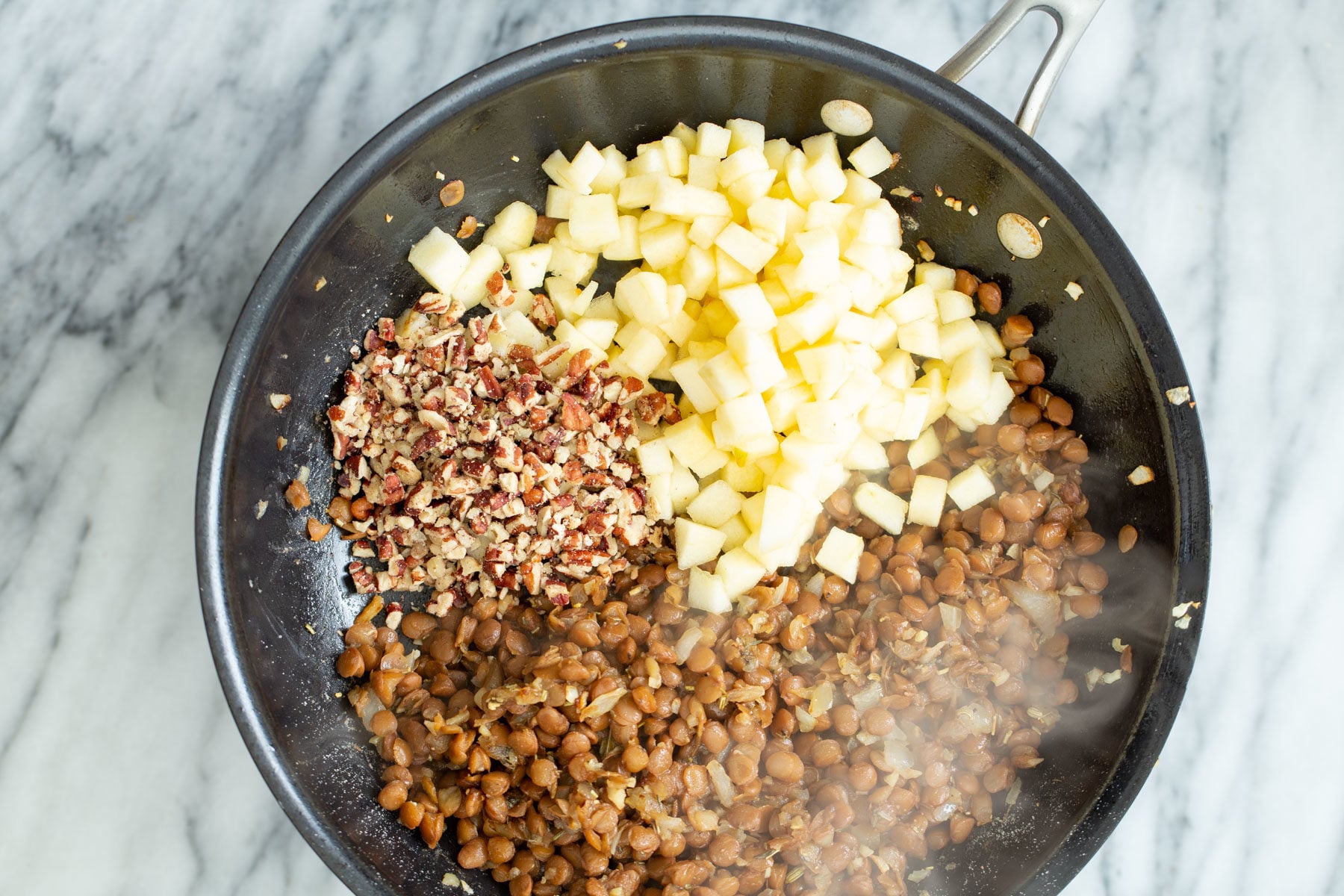 vegan stuffed butternut squash apples and chopped nuts being added to vegan lentil stuffing in a frying pan