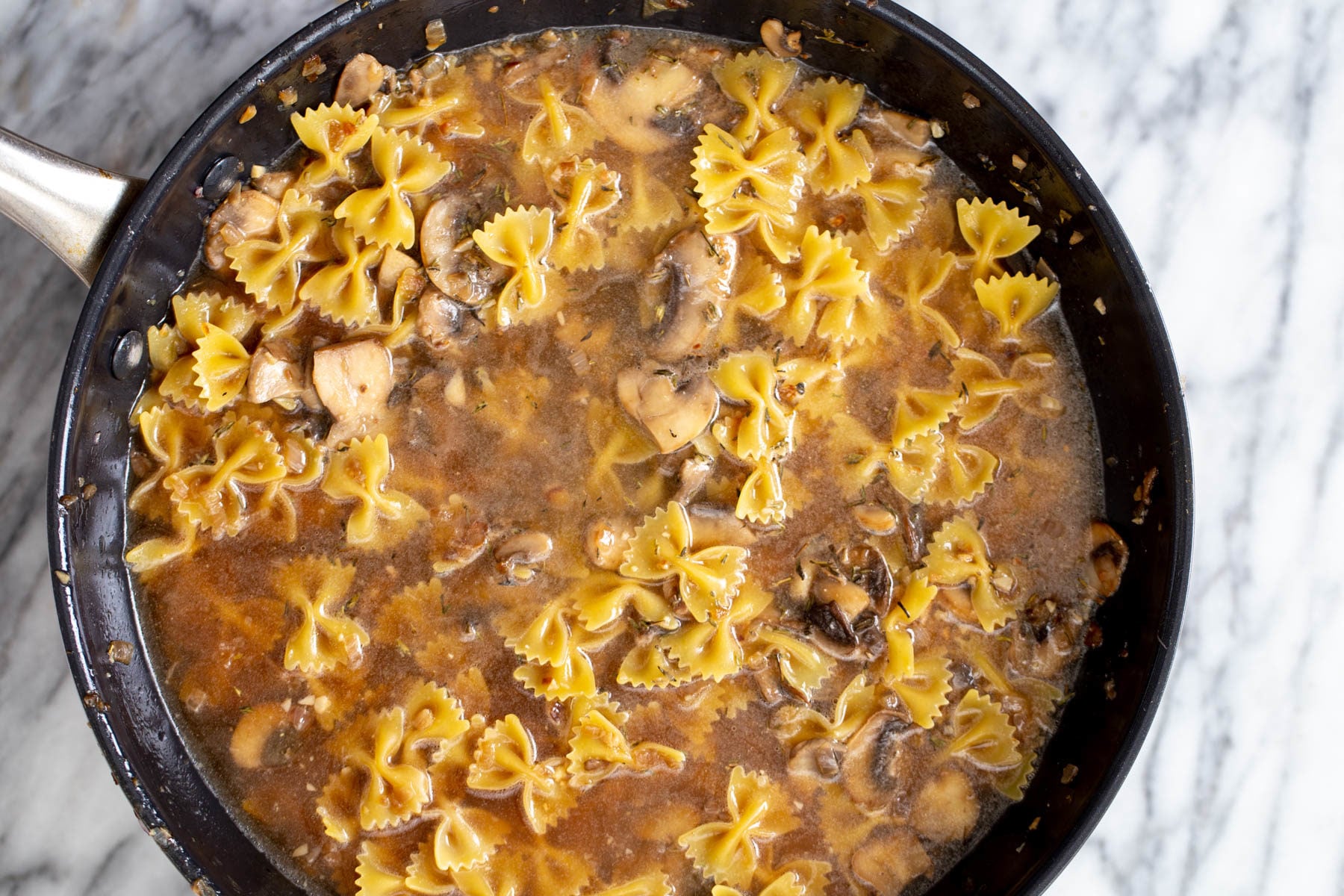 vegan mushroom stroganoff uncooked farafalle pasta and mushroom sauce cooking in a saucepan