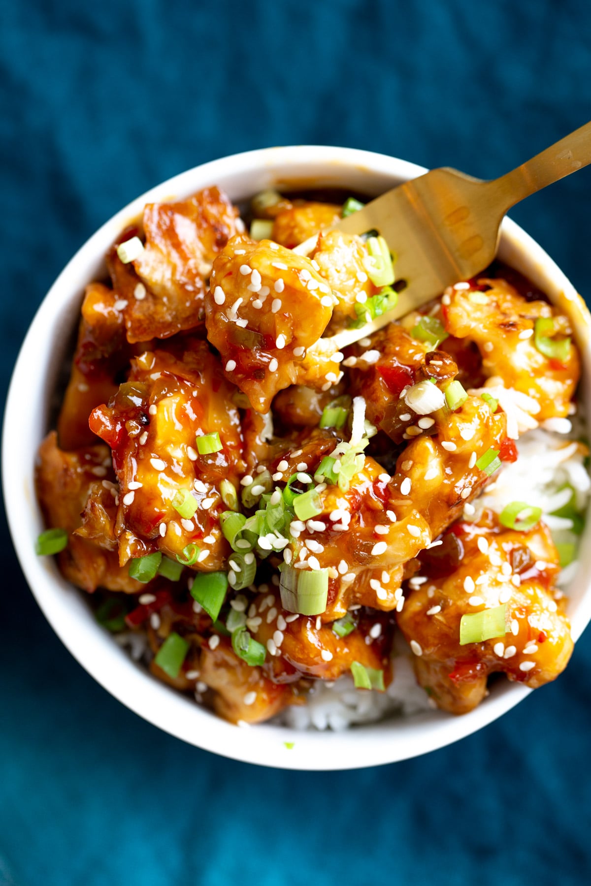 a fork digging into a serving of baked vegan general tso cauliflower served over rice