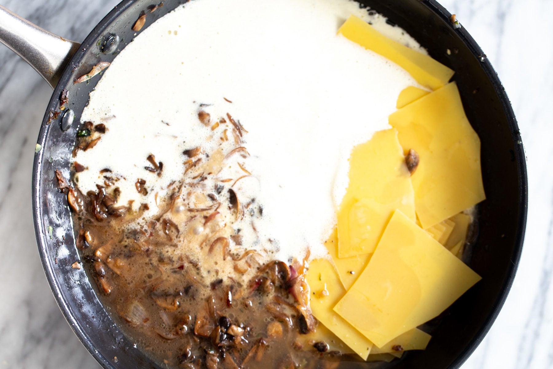 alfredo sauce and lasagna sheets being added to skillet to make skillet lasagna