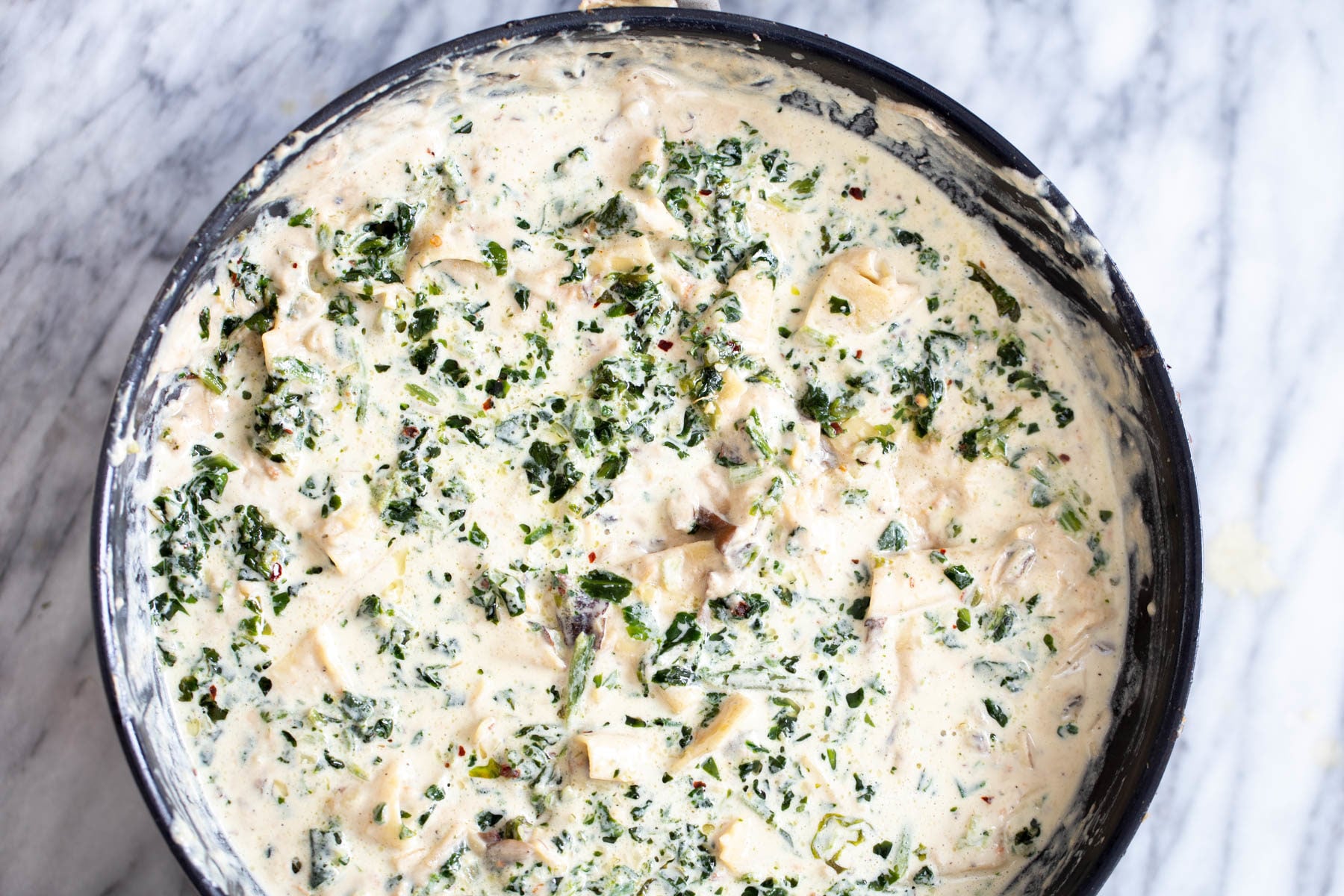 overhead shot of a black skillet with cooked lasagna noodles in vegan alfredo sauce with mushrooms and spinach