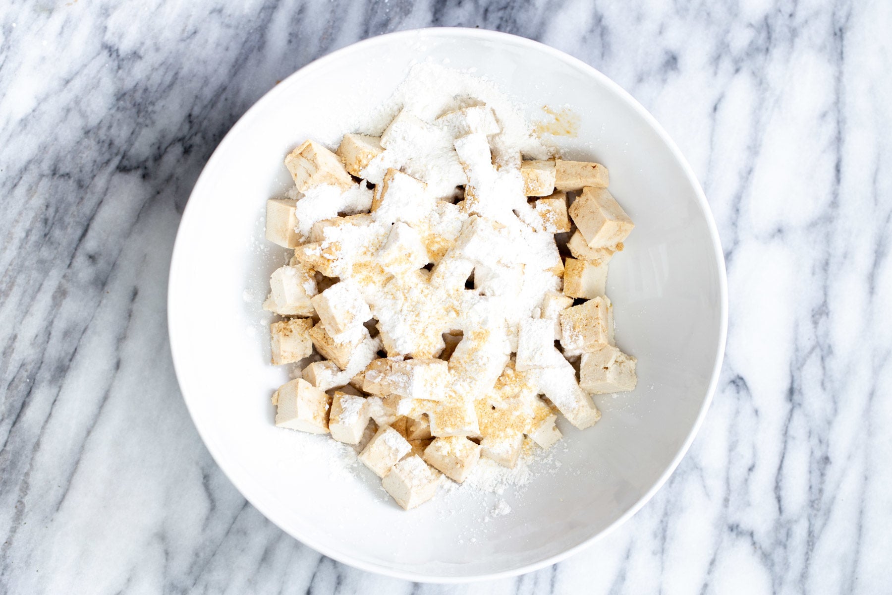 marinated tofu cubes being tossed with cornflour in a bowl