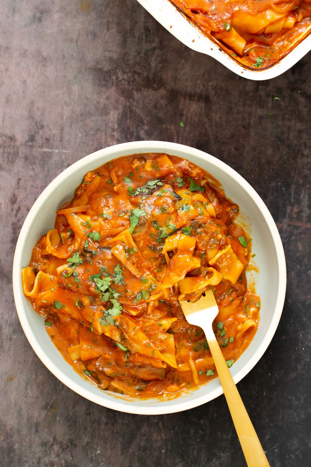 a bowl filled with vegan butter chicken lasagna with a fork sticking in