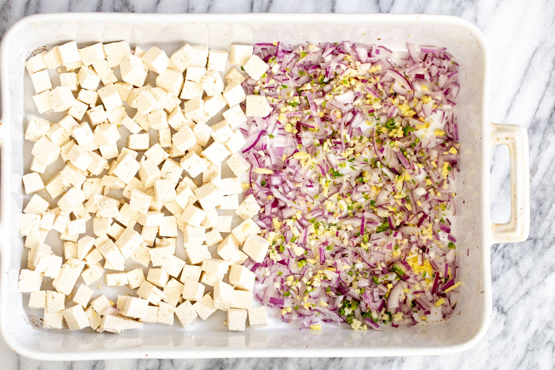 baked tofu curry tofu cubes in a casserole dish next to minced onion, ginger, garlic and chile